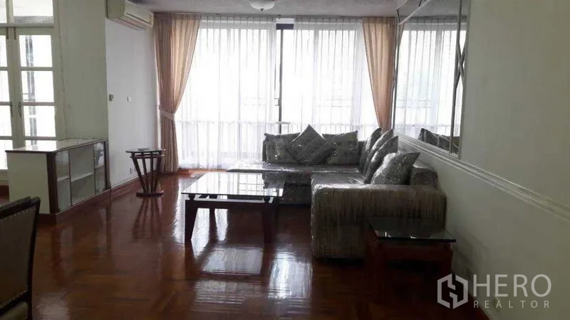 อพาร์ทเมนท์ ให้เช่าในPathum Wan, Bangkok - ห้องนั่งเล่นสว่าง โซฟาเข้ามุม โต๊ะกลางกระจก พื้นปาร์เกต์ และผ้าม่านสูงจรดเพดาน