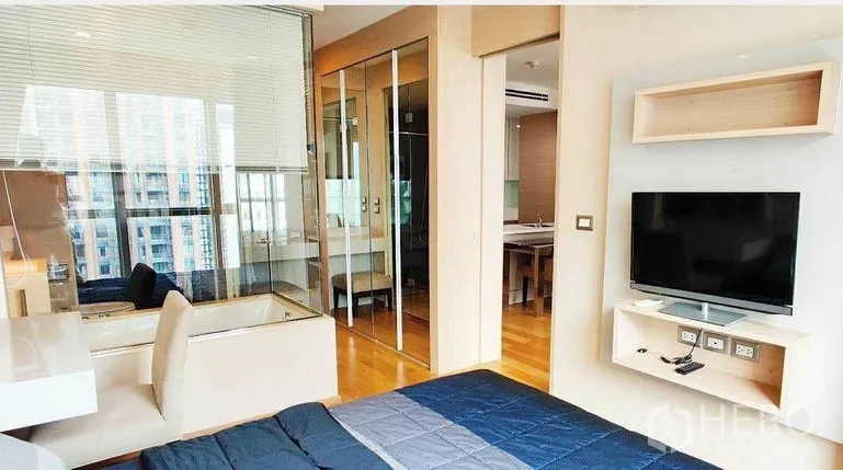 คอนโด ให้เช่าในRatchathewi, Bangkok - มุมห้องนอนมีทีวีติดผนัง ฉากกั้นกระจกเชื่อมห้องน้ำ โต๊ะทำงานบิวท์อิน พื้นไม้