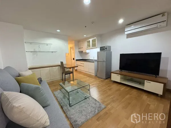 公寓 出租在Khlong Toei, Bangkok - 开放式客厅配电视、空调、精巧厨房与玻璃茶几。