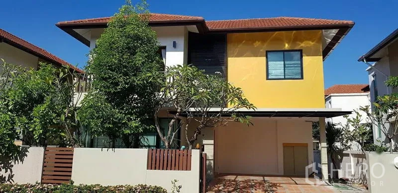 Detached House for rent in Bang Phli, Samut Prakan - Modern two-storey detached house with yellow accent facade, tiled roof, trees and a covered carport.