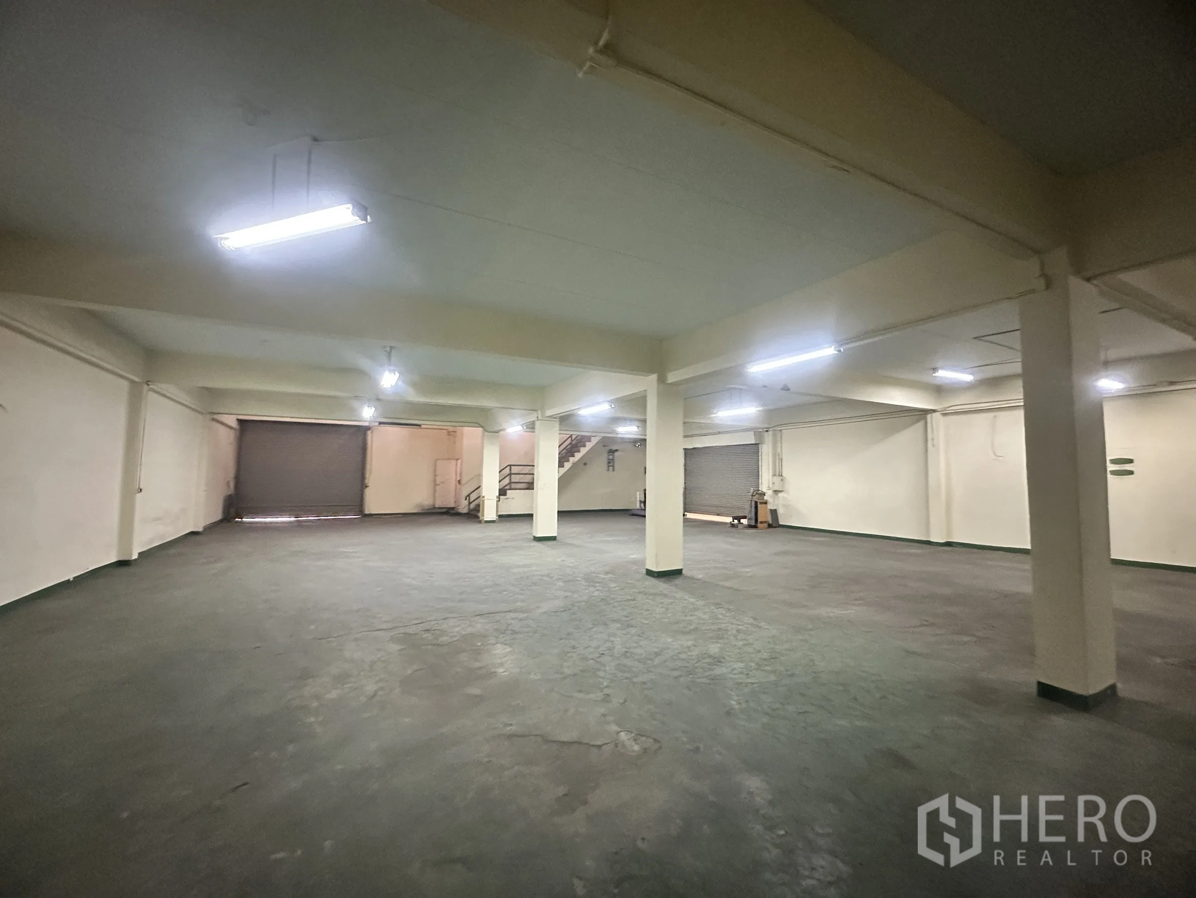 Factory for sale in Bang Bua Thong, Nonthaburi - Open warehouse floor with fluorescent lighting and roller shutter doors.