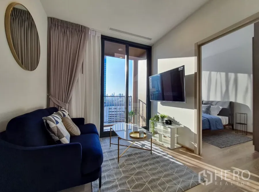 คอนโด ให้เช่าในKhlong Toei, Bangkok - ห้องนั่งเล่นรับแสง พร้อมโซฟาสีน้ำเงิน ทีวีติดผนัง และระเบียงวิวเมือง