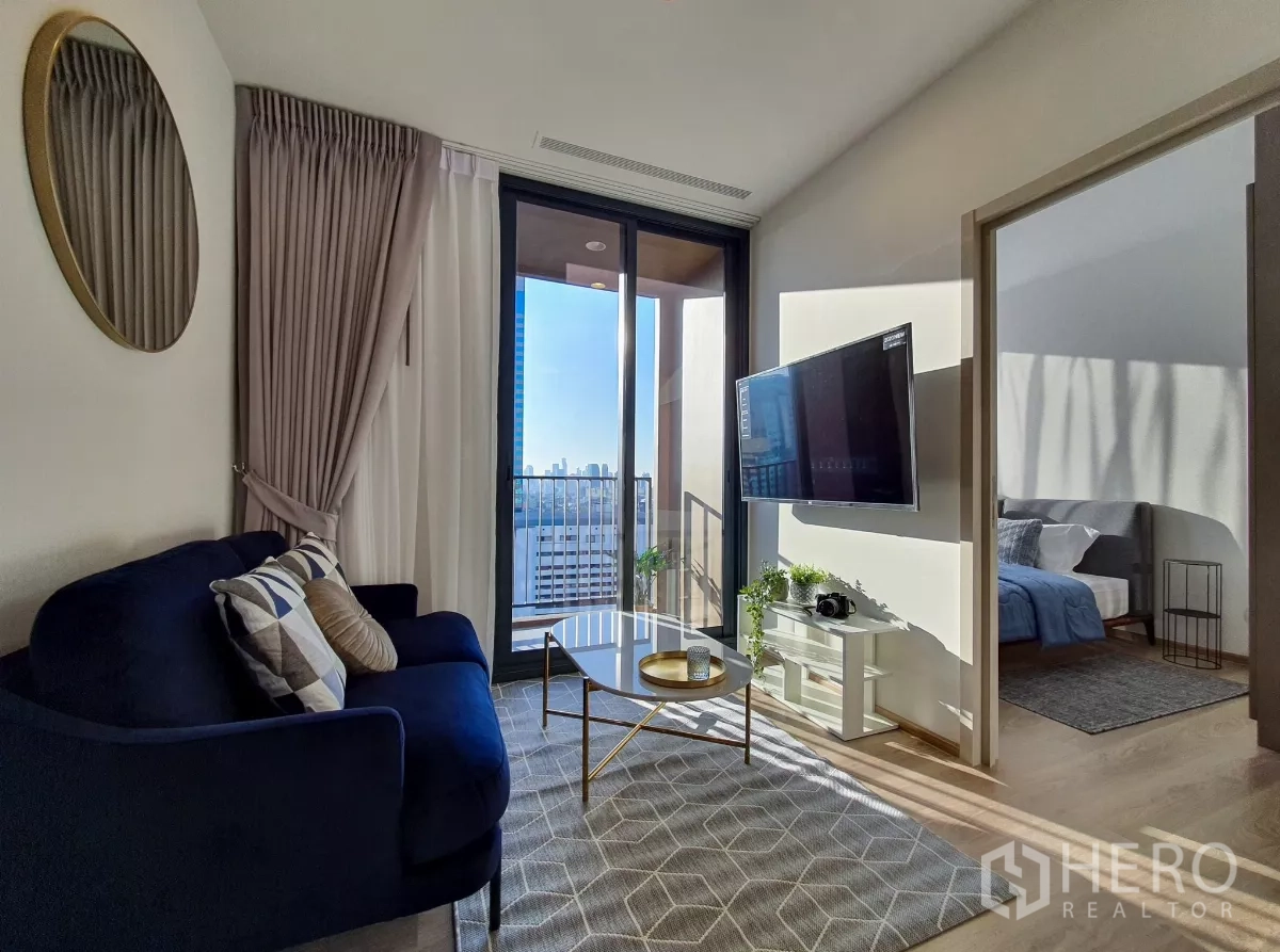 คอนโด ให้เช่าในKhlong Toei, Bangkok - ห้องนั่งเล่นรับแสง พร้อมโซฟาสีน้ำเงิน ทีวีติดผนัง และระเบียงวิวเมือง