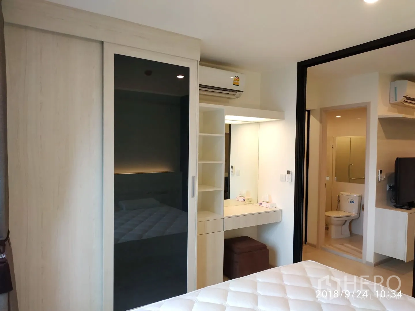 Condominium for rent in Huai Khwang, Bangkok - Bedroom with sliding-door wardrobe, vanity and air conditioner, with doorway to the bathroom.