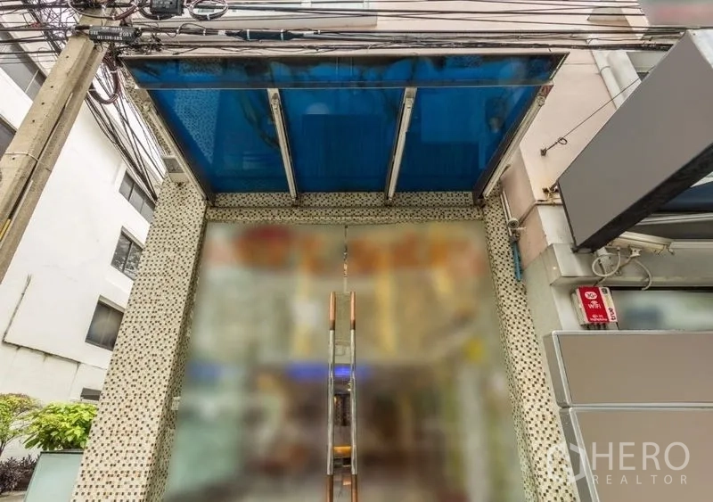 พื้นที่ขายปลีก ให้เช่า - ทางเข้าอาคารกระจกพร้อมกันสาดสีน้ำเงินและประตูคู่ บนทำเลในกรุงเทพฯที่คึกคัก