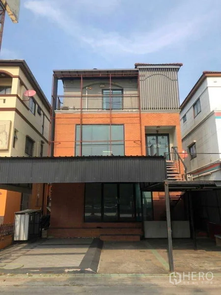 Home Office for sale in Min Buri, Bangkok - Three-storey brick-and-metal home office with large glass windows, balcony terrace, external stair and covered parking.