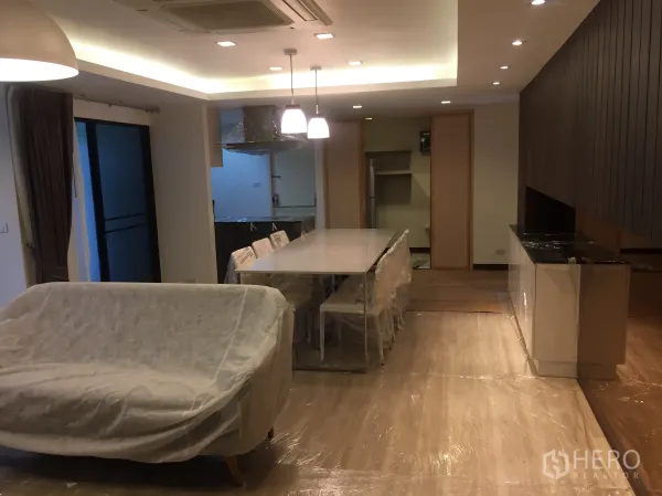 Condominium for rent in Pathum Wan, Bangkok - Open-plan living and dining area with long dining table, pendant lights and sliding door to balcony.