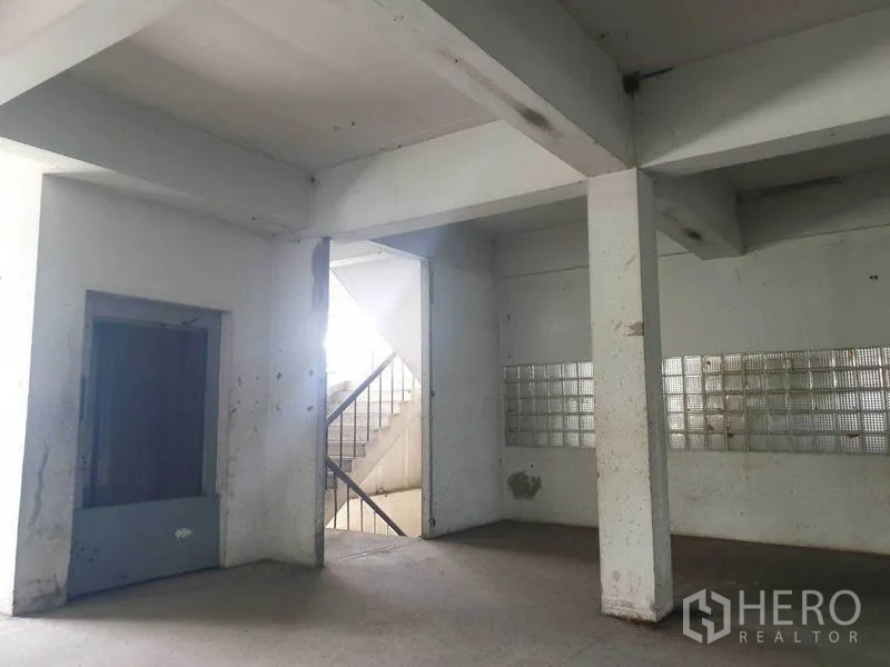 Shophouse for rent in Bang Bo, Samut Prakan - Ground floor corner showing pillars, stairwell and glass-block wall inside a shophouse.