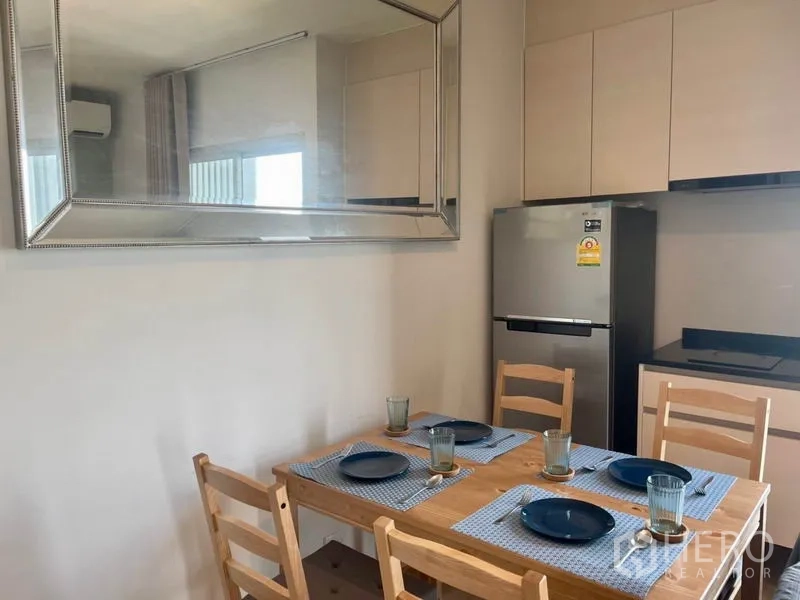 Condominium for rent in Huai Khwang, Bangkok - Close-up of wooden dining table set with plates under large wall mirror.