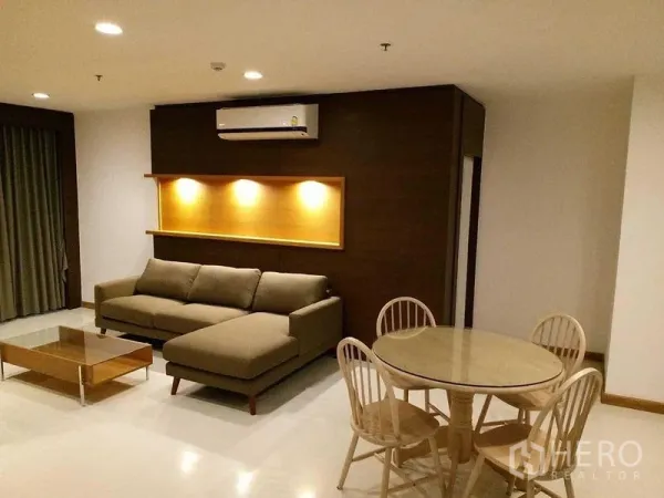 Condominium for rent in Sathon, Bangkok - Spacious living room with L-shaped sofa, spotlighted feature shelf, air conditioner, and round dining set.