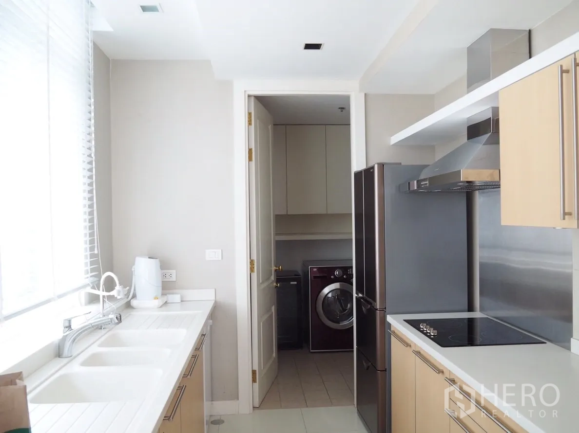 Condominium for rent in Pathum Wan, Bangkok - Modern enclosed kitchen with double sinks, electric cooktop, stainless refrigerator and a laundry room with a washing machine.