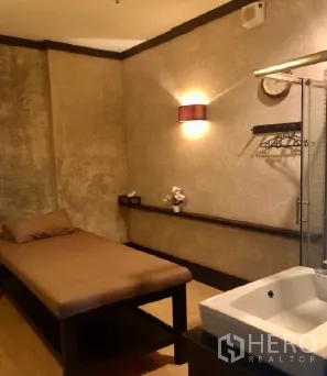 零售空间 出租在Pathum Wan, Bangkok - 室内温暖灯光的功能房，配按摩床、壁灯与洗手台，适合美容、诊所或沙龙。