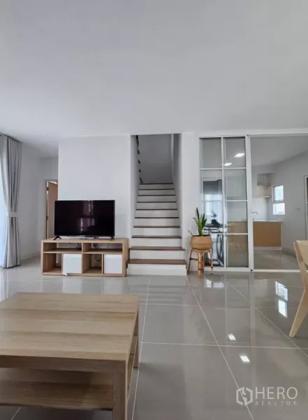Detached House for rent in Bang Phli, Samut Prakan - Bright living room with TV stand, staircase and sliding glass door to the kitchen.