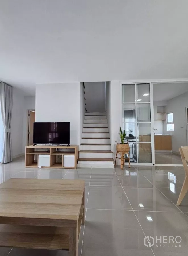 Detached House for rent in Bang Phli, Samut Prakan - Bright living room with TV stand, staircase and sliding glass door to the kitchen.