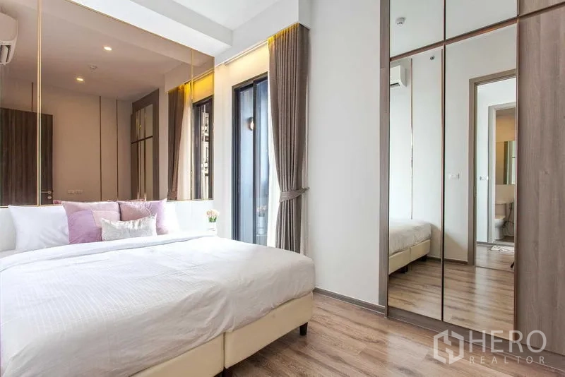 Condominium for rent in Watthana, Bangkok - Bedroom with mirrored wardrobe, balcony-style door, soft curtains and wood flooring.