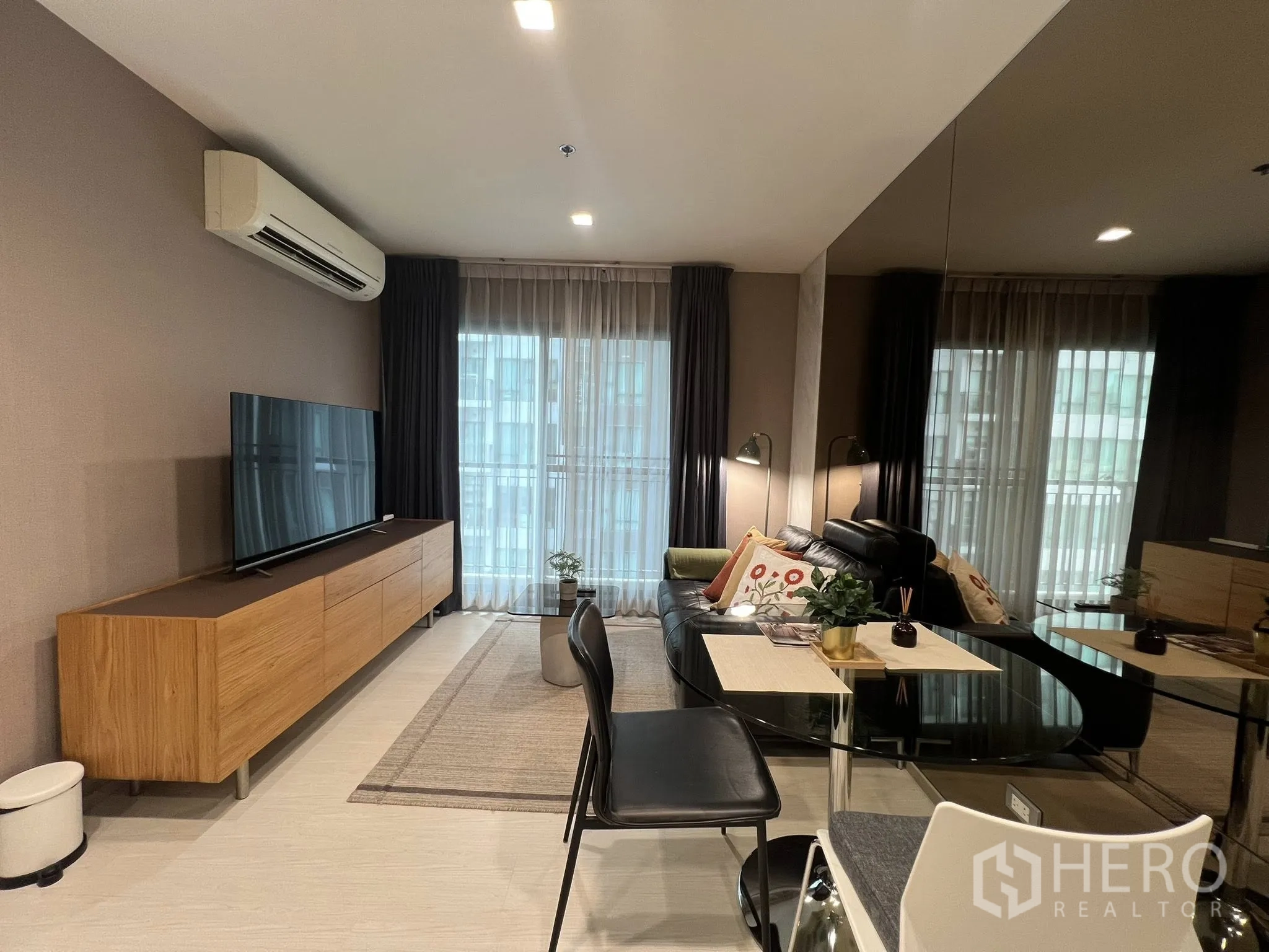 Condominium for rent in Khlong Toei, Bangkok - Contemporary living room with leather sofa, large TV, dining set, and floor-to-ceiling windows.