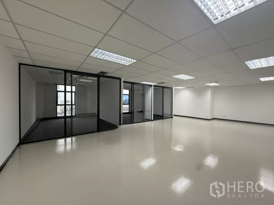 Office Space for rent - Spacious open-plan Bangkok office with glass-partitioned rooms, bright grid ceiling lights, and glossy flooring.