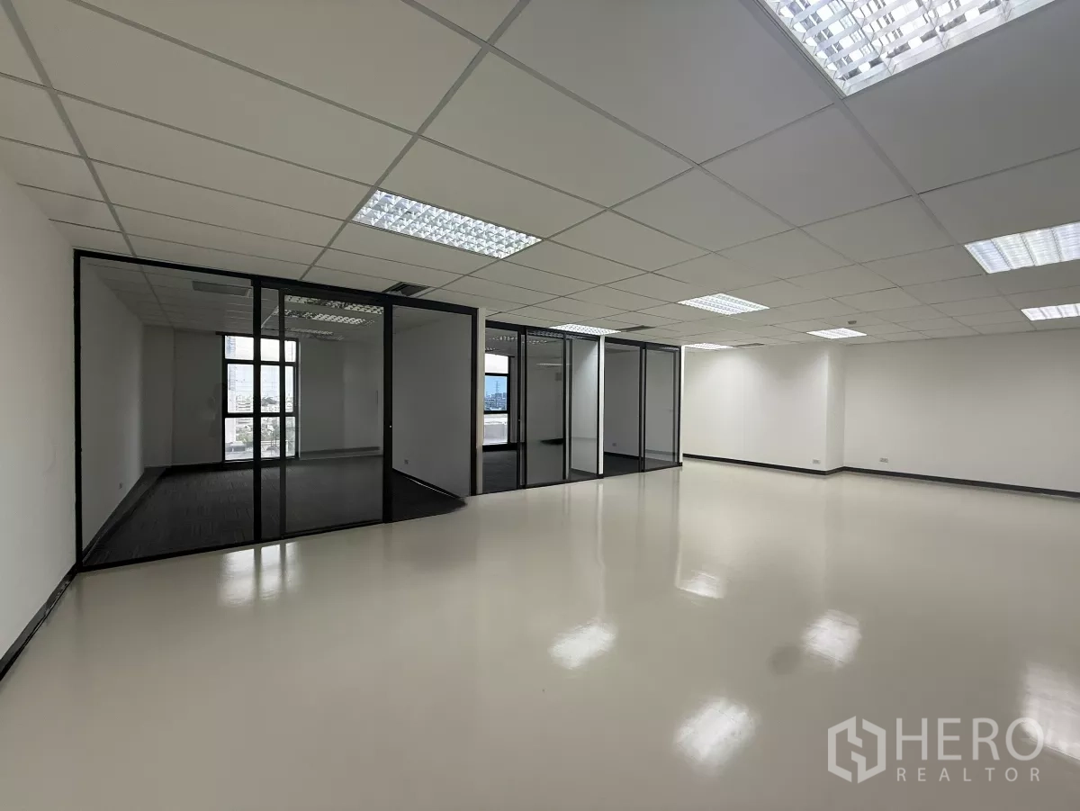 Office Space for rent - Spacious open-plan Bangkok office with glass-partitioned rooms, bright grid ceiling lights, and glossy flooring.