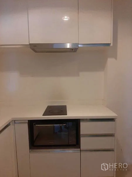 Condominium for rent or sale in Huai Khwang, Bangkok - Compact kitchen corner with cooktop, built-in microwave and white cabinetry.