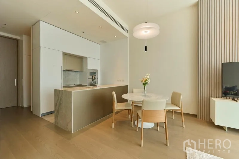Condominium for rent in Pathum Wan, Bangkok - Minimalist open kitchen with an island beside the dining area in a light wood interior.