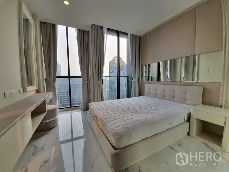 Condominium for rent in Pathum Wan, Bangkok - Bright bedroom with full-height windows, city skyline view and a dressing table.