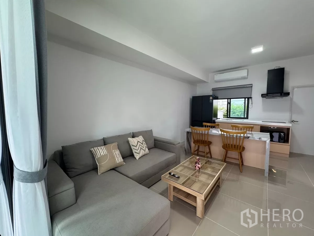 Townhouse for rent in Bang Phli, Samut Prakan - Open-plan living room with gray sectional sofa and breakfast bar kitchen