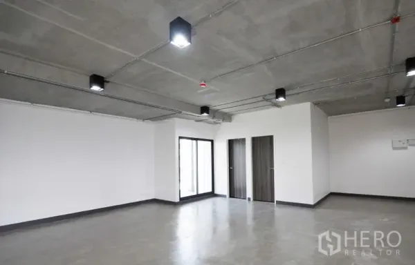 Office Space for rent in Watthana, Bangkok - Spacious office area with sliding glass door, two internal doors for storage or restrooms, and an industrial-style exposed ceiling.