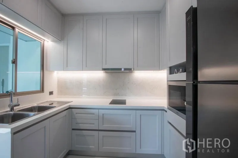 Detached House for sale in Saphan Sung, Bangkok - L-shaped modern kitchen with white cabinetry, double sink and stainless appliances.