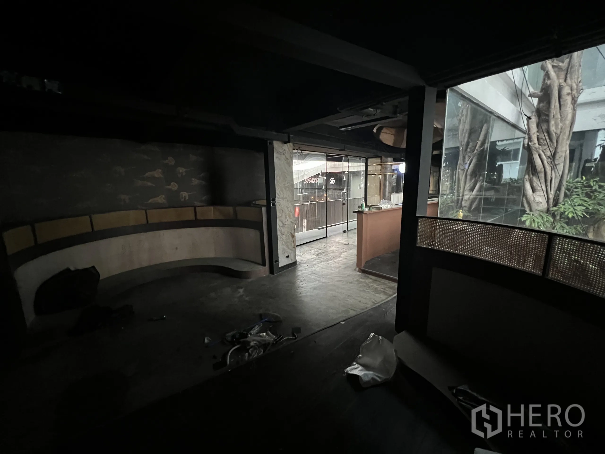 零售空间 出租在Watthana, Bangkok - 室内走道带弧形卡座，玻璃外望庭院大树。