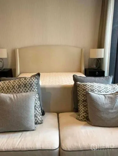 คอนโด ให้เช่าในPathum Wan, Bangkok - ห้องนอนตกแต่งอบอุ่น มีหัวเตียงบุผ้า โต๊ะข้างพร้อมโคมไฟ และโซฟาพร้อมหมอนลายเรขาคณิต