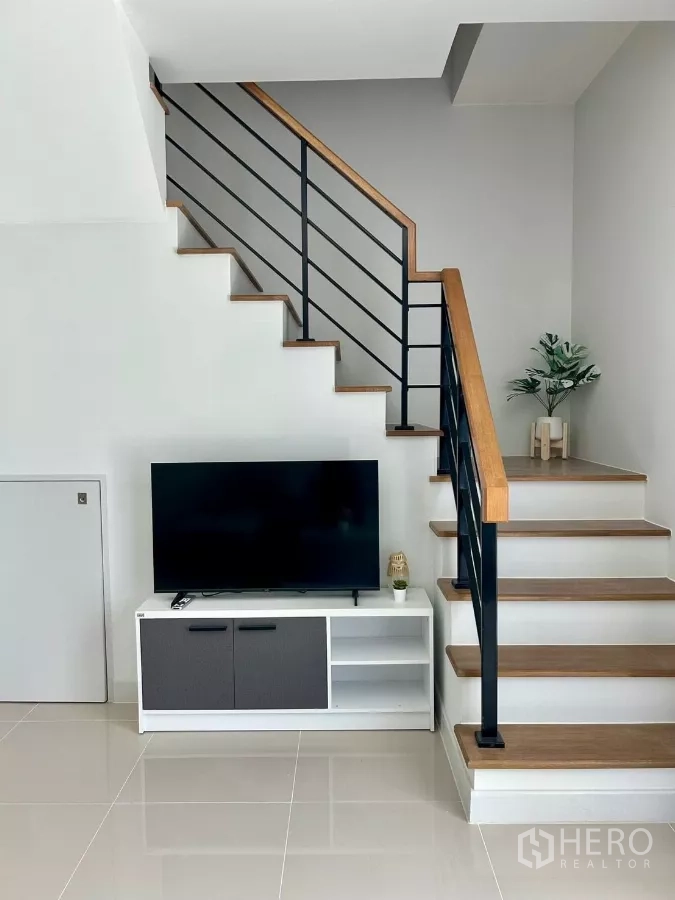 Townhouse for rent in Bang Phli, Samut Prakan - Wood-and-metal staircase beside TV console in a minimalist living area.