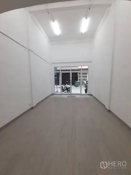 店屋 出租在Khlong Toei, Bangkok - 一层明亮的商铺空间，挑高白墙、木纹地面，整面玻璃门面临街