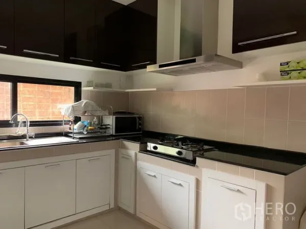 Detached House for rent or sale in Khan Na Yao, Bangkok - L-shaped kitchen with gas hob, range hood, white cabinets and black countertops.