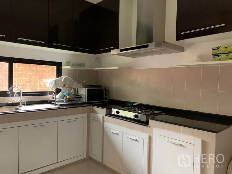 Detached House for rent or sale in Khan Na Yao, Bangkok - L-shaped kitchen with gas hob, range hood, white cabinets and black countertops.
