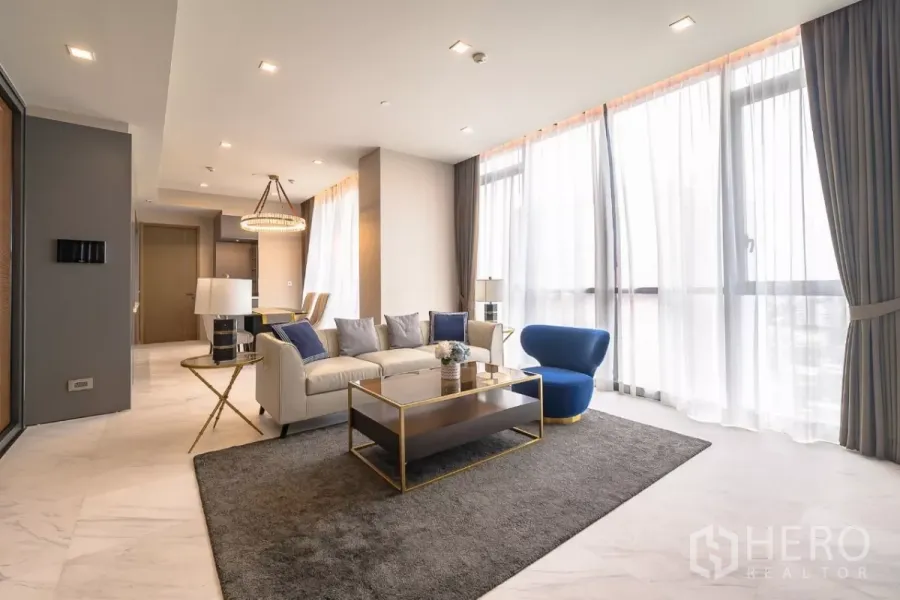 公寓 出租在Watthana, Bangkok - 采光充足的客厅，落地纱帘、米色沙发、蓝色单椅、金属茶几与吊灯。