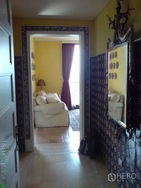 Condominium for rent in Khlong Toei, Bangkok - Hallway with patterned tile walls and mirror leading to a bright lounge with balcony.