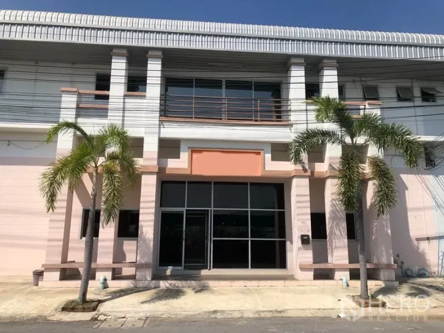 工厂 出租在Pak Kret, Nonthaburi - 帕克雷特两层工厂外立面，玻璃入口与阳台，门前种有棕榈树。