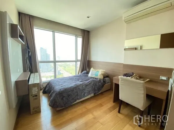 Condominium for sale in Ratchathewi, Bangkok - Bright bedroom with desk and floor-to-ceiling window showcasing Bangkok skyline views.