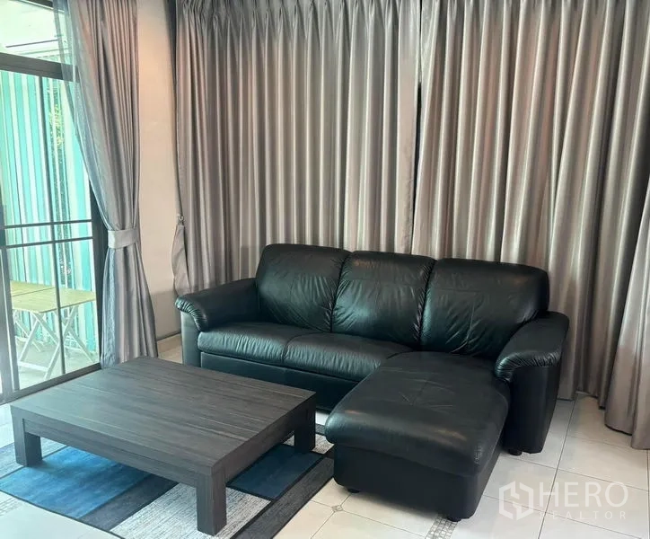 Detached House for rent in Bang Phli, Samut Prakan - Black leather L-shaped sofa and coffee table in front of floor-to-ceiling curtains.