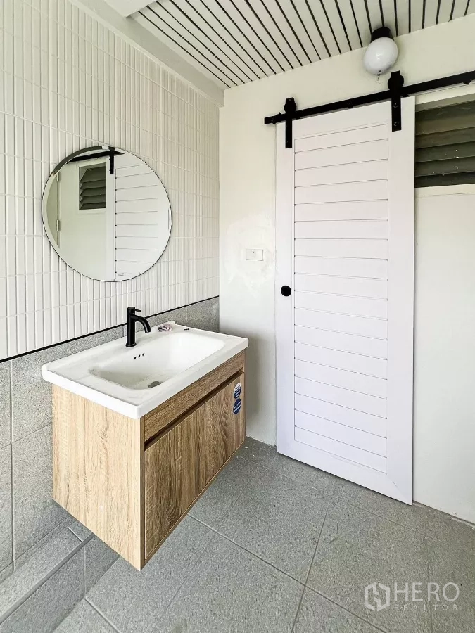 Townhouse for rent - Renovated wash area with wood-look vanity, round mirror and white sliding barn door.