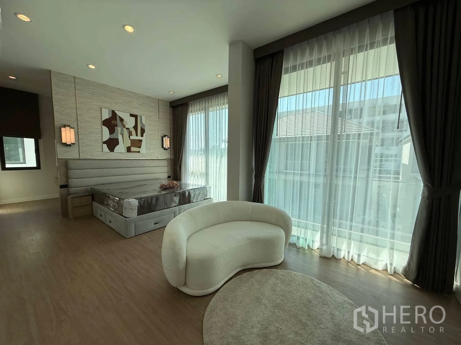 Detached House for rent in Bang Phli, Samut Prakan - Expansive master bedroom with upholstered headboard, artwork, curved sofa, and wide windows with curtains.