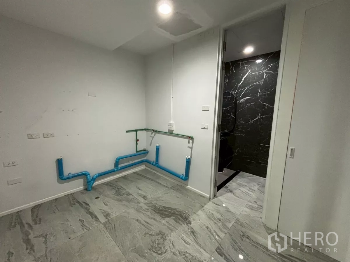 Condominium for sale in Bang Kho Laem, Bangkok - Utility room with exposed blue plumbing ready for kitchen or laundry beside a black marble bathroom.