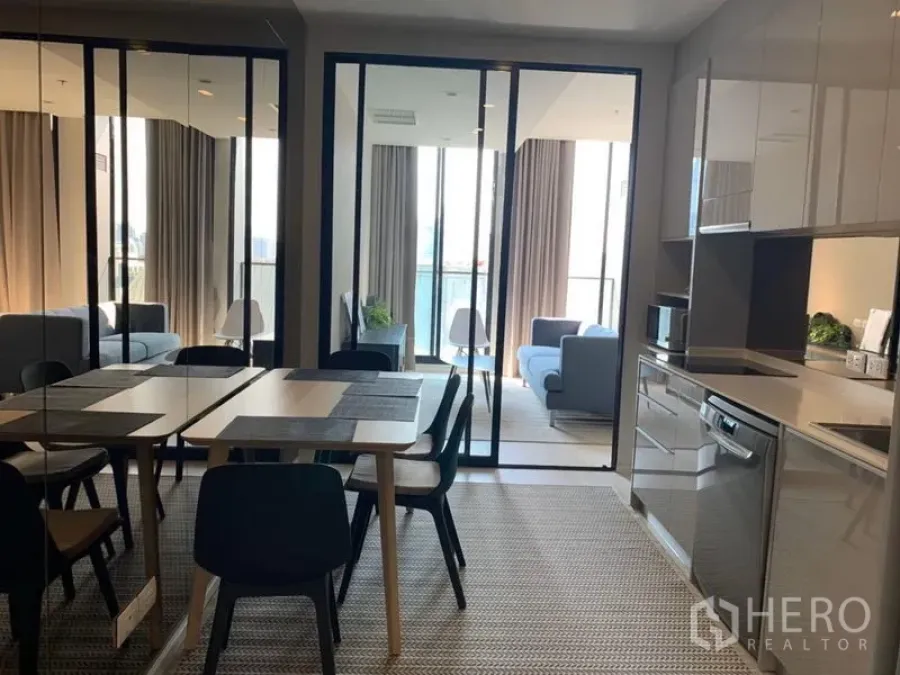 公寓 出租在Pathum Wan, Bangkok - 开放式餐区与亮面橱柜厨房，玻璃推门通向明亮客厅