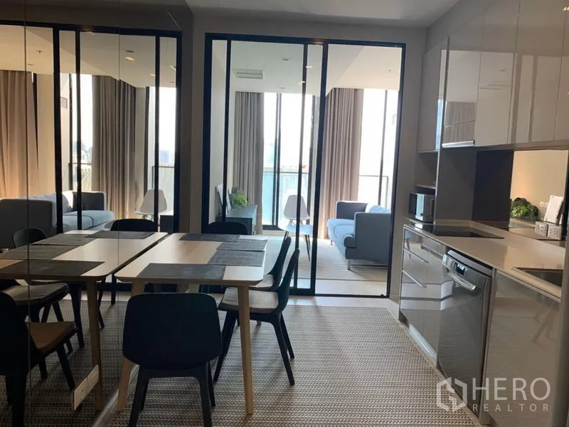 公寓 出租在Pathum Wan, Bangkok - 开放式餐区与亮面橱柜厨房，玻璃推门通向明亮客厅