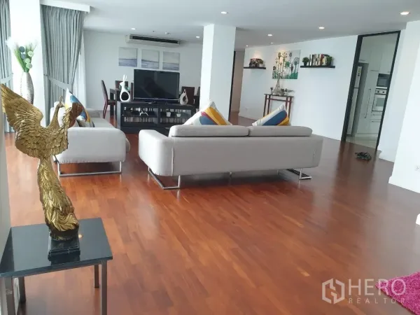 Apartment for rent in Bang Rak, Bangkok - Spacious open living room with two sofas, TV cabinet and dining area on wood flooring.