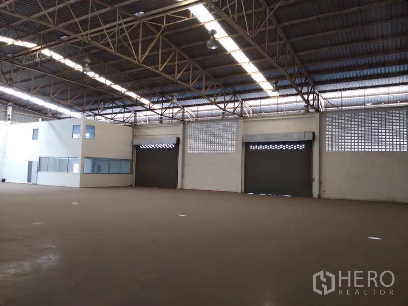 Warehouse for rent in Bang Phli, Samut Prakan - Open warehouse hall with steel truss roof, three roller shutter doors and an attached office box.