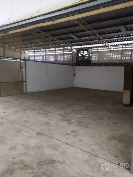 Warehouse for rent in Suan Luang, Bangkok - Semi-open loading bay with concrete floor, mesh partitions and an industrial exhaust fan.