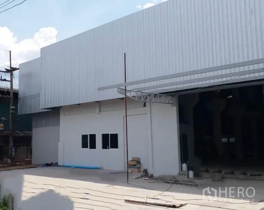 Factory for rent in Krathum Baen, Samut Sakhon - Front view of metal-clad factory building with wide driveway and large open entrance for loading.