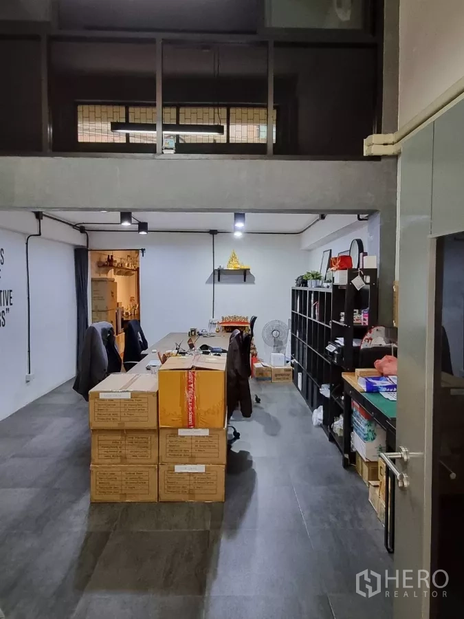 Home Office for rent in Pom Prap Sattru Phai, Bangkok - Open‑plan workspace with mezzanine storage, long workbench and shelving units.