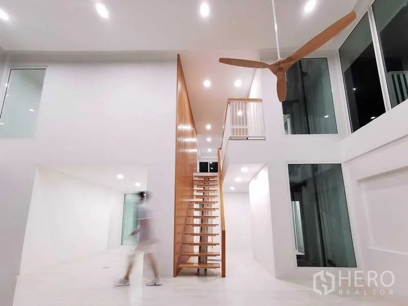 Home Office for sale in Suan Luang, Bangkok - Minimalist double-height hall with an open wooden staircase and large ceiling fan.